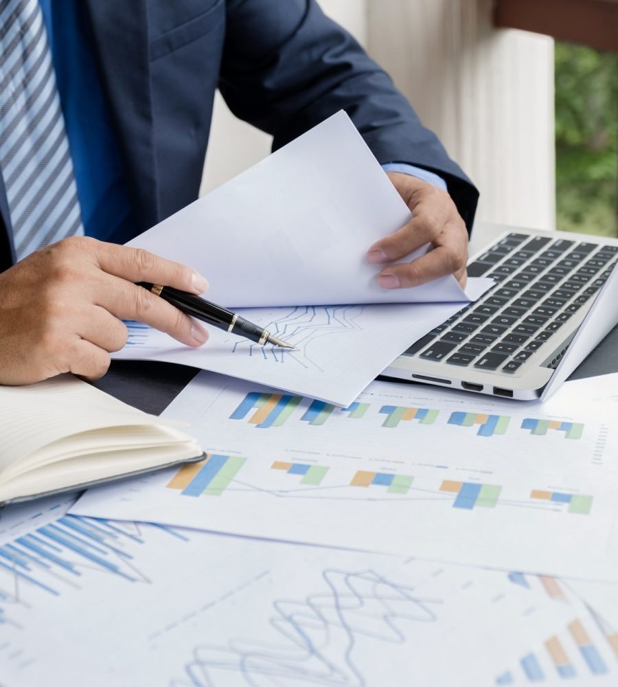 businessman-hand-holding-pen-analysis-the-graph-with-laptop-at-the-home-office.jpg